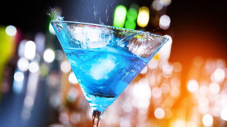 blue drink in a martini glass with blurred lights in the background