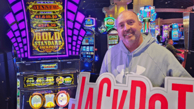 Man holding Jackpot sign in front of gaming machine. 