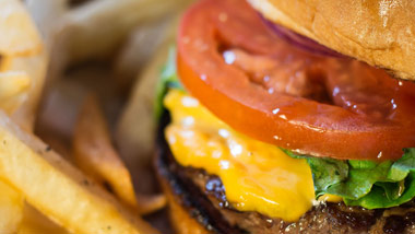 close up picture of a cheeseburger with tomato and lettuce and french fries